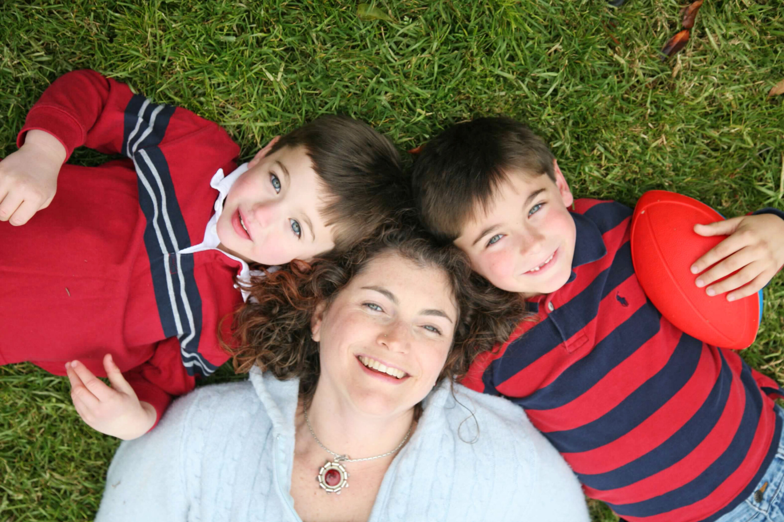 Photo of a mother with her two sons laying down on the grass.